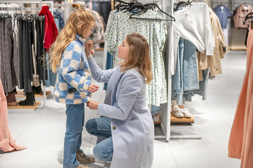 Mom and daughter in a store trying on warm coats.